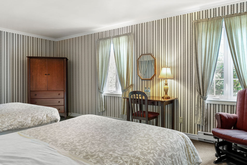Room with two beds, windows and a writing desk at Auberge du Manoir