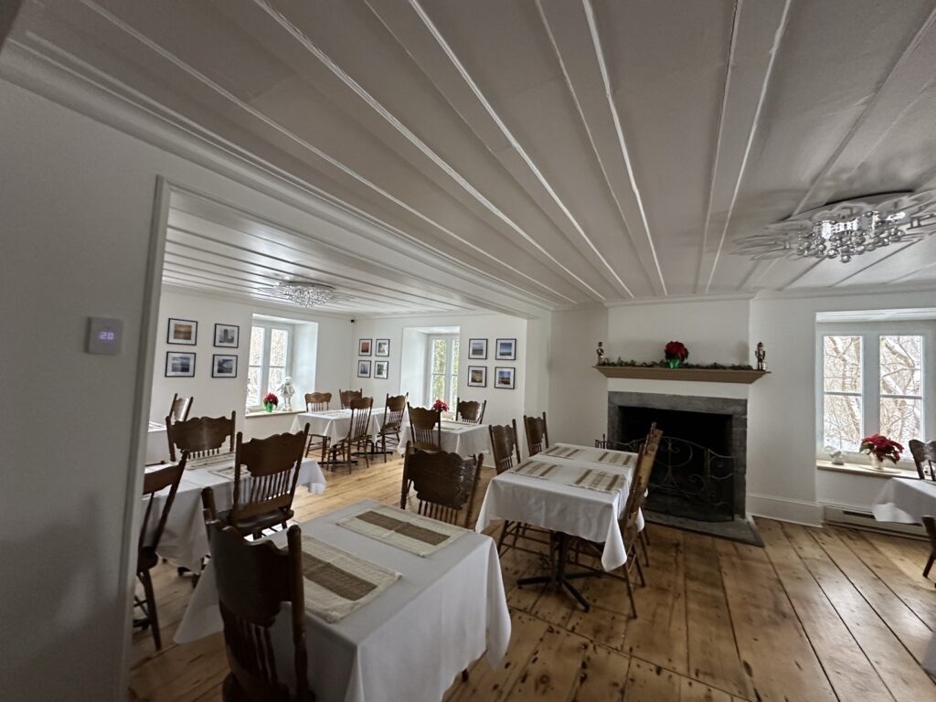 Dining room at Auberge du Manoir with tablecloth-covered tables and a fireplace.