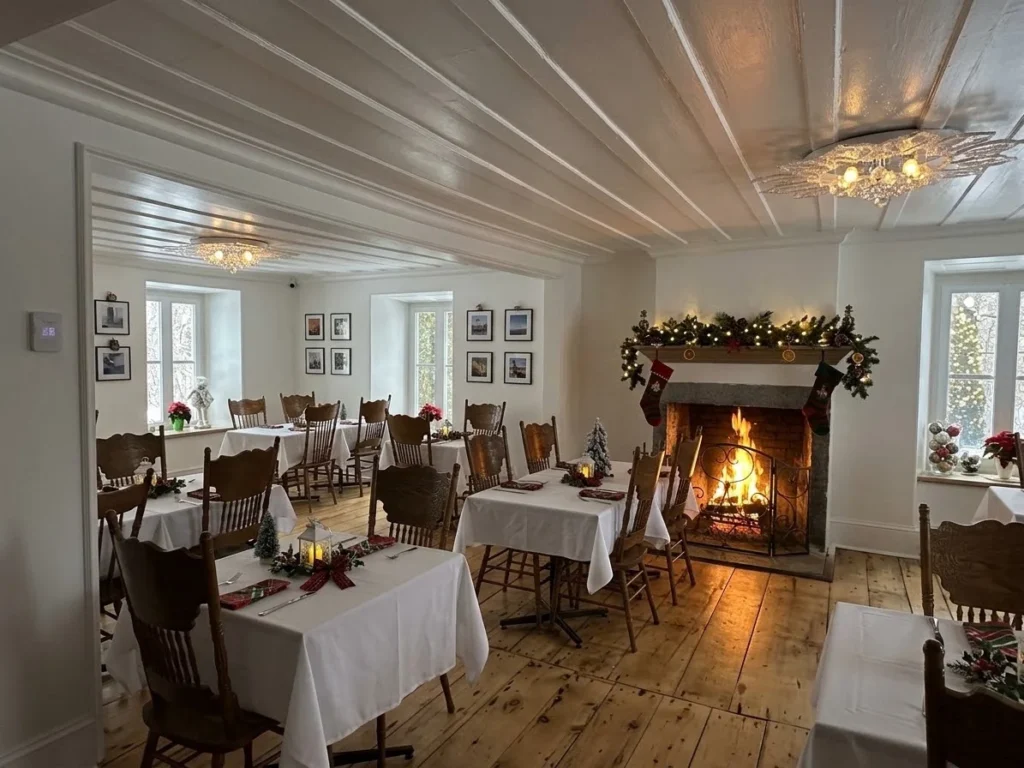 Bright dining room at Auberge du Manoir with small tables and a lit fireplace